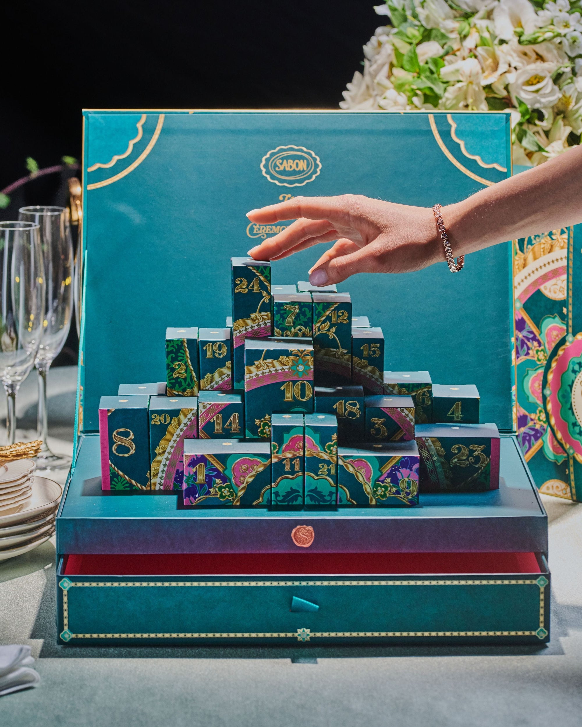 Advent calendar with colorful boxes being opened by a hand against a teal background